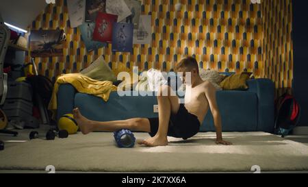 Il giovane atleta usa un rullo in schiuma nella sua stanza. Scaldare gli allenamenti sportivi. Scuola sport squadra giocatore di calcio. Stretching muscoli. Allenati a casa. Foto Stock