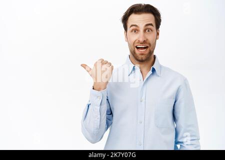 Bell'uomo d'affari sorridente che punta a sinistra, mostrando promo o banner aziendale da parte, dimostrando la pubblicità, sfondo bianco Foto Stock