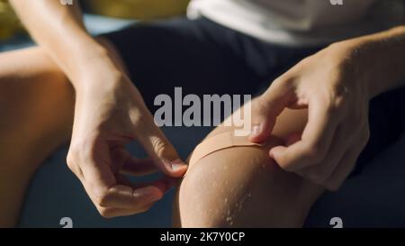 Ragazzo adolescente che applica cerotto adesivo medico sul ginocchio. Pronto soccorso dopo una lesione. Tagli, abrasioni e ferite leggermente sanguinanti durante lo sport concept. Foto Stock