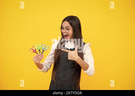 Creatività, arte e artigianato per bambini. Ragazza adolescente con forbici, isolata su sfondo giallo. Foto Stock