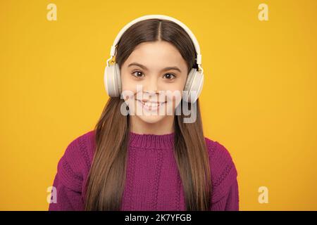 Adolescente in moderne cuffie wireless che ascolta la musica delle canzoni nell'app audio, ascoltando la sua musica preferita su sfondo giallo dello studio. Foto Stock