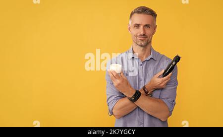 dopo la rasatura. uomo che tiene il rasoio elettrico e la crema. ragazzo grizzled che presenta il rasoio elettrico. Foto Stock