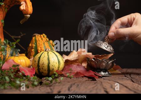 La mano di una donna mette il fuoco su un bastone di incenso su un bruciatore. Sfondo per il giorno d'autunno. Foto Stock