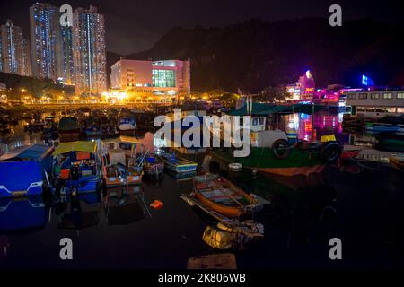 Barche da pesca ormeggiate di notte nel rifugio del tifone, con alti blocchi residenziali e ristoranti di pesce oltre, lei Yue Mun, Kowloon, Hong Kong Foto Stock