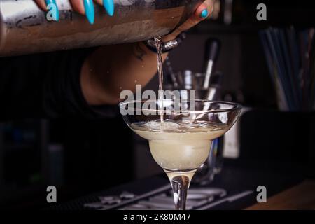 La ragazza barista versa il cocktail in un bicchiere. Primo piano. Foto Stock