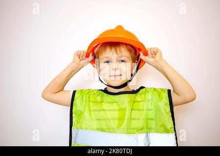 un ragazzo in un casco e un giubbotto sta reggendo su un casco. un piccolo operaio. il ragazzo è un costruttore. Foto Stock