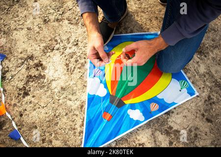 un uomo lega una corda su un aquilone di un bambino. legando un aquilone. preparandosi per il volo Foto Stock