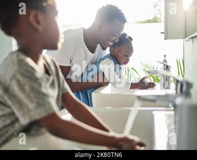 Creare una routine di igiene personale per i suoi figli. Un padre aiuta i suoi figli a lavarsi le mani in un bagno a casa. Foto Stock