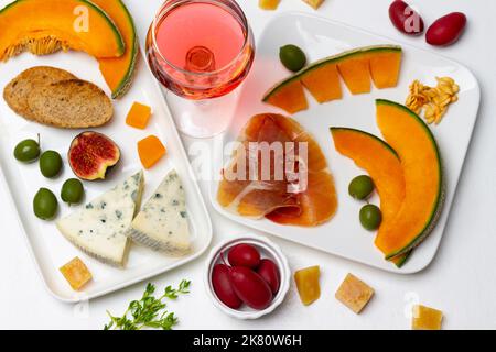 Aperitivo con olive, fettine di melone, fichi, formaggio e vino rosso. Giacitura piatta. Sfondo bianco. Foto Stock