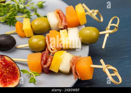 Spiedini con formaggio, olive e jamon su piatto grigio. Primo piano. Sfondo blu. Foto Stock