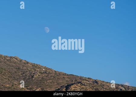 Vista di una montagna con una singola cappella bianca e la luna nel cielo blu in Grecia iOS Foto Stock