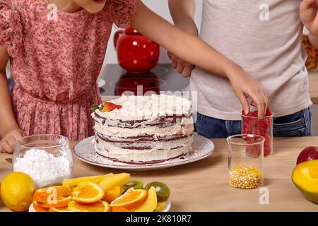 Piccoli amici stanno facendo una torta insieme ad una cucina contro una parete bianca con gli scaffali su esso. Foto Stock