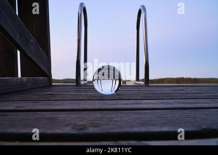 Palla di vetro su un molo di legno presso un lago svedese all'ora serale. Foto della natura dalla Scandinavia Foto Stock