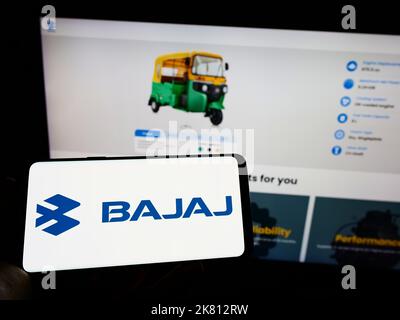 Persona che tiene il cellulare con il logo della società automobilistica indiana Bajaj Auto Limited sullo schermo di fronte al sito web aziendale. Messa a fuoco sul display del telefono. Foto Stock