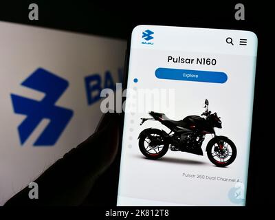 Persona che tiene il cellulare con il Web page dell'azienda automobilistica indiana Bajaj Auto Limited sullo schermo con il marchio. Messa a fuoco al centro del display del telefono. Foto Stock