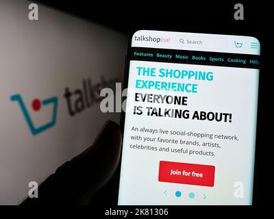 Persona che tiene il cellulare con il Web page della società americana di vendita sociale TalkShopLive Inc. Sullo schermo di fronte al logo. Messa a fuoco al centro del display del telefono. Foto Stock