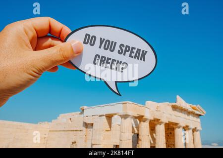 Un uomo tiene un segno a forma di bolla di discorso con la domanda si parla greco scritto in esso, di fronte al Partenone, nell'Acropoli di Foto Stock