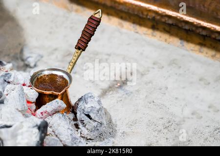Il caffè macinato naturale viene preparato in turk di rame su carboni secondo la tradizione turca, primo piano, copia spazio Foto Stock