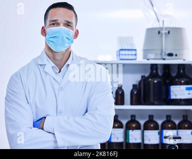 Puoi fidarti di me. Ritratto corto di un giovane scienziato maschio che indossa una maschera mentre si trova in piedi con le braccia ripiegate nel suo laboratorio. Foto Stock