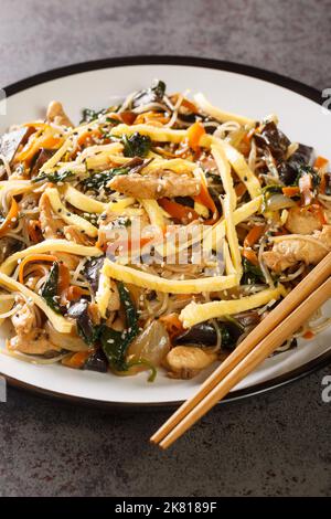 Japchae Korean Glass spolverare con uova, verdure e funghi primo piano sul piatto sul tavolo. Verticale Foto Stock