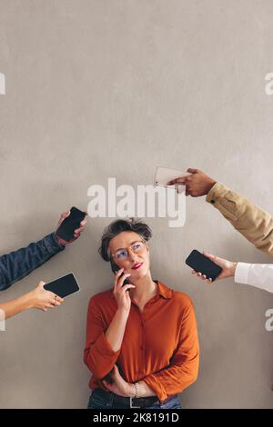 Donna d'affari matura che parla al telefono mentre è circondata da mani che tengono gli smartphone. Professionista di affari femminile che risponde alle telefonate in un occupato Foto Stock