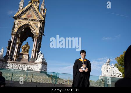 Un giovane laureato asiatico presso l'Imperial College celebra il suo successo educativo con amici e famiglie sotto l'Albert Memorial dopo la cerimonia di laurea presso la Royal Albert Hall, il 19th ottobre 2022, a Londra, Inghilterra. Foto Stock