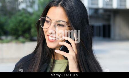 Primo piano di una donna di affari latina sorridente con gli occhiali che parlano sul telefono delle cellule. Foto Stock