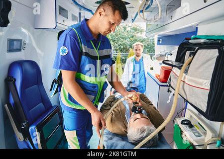 Pronto soccorso, ambulanza. Assistente di cura dell'ambulanza che fornisce l'aiuto medico con la maschera artificiale di ventilazione polmonare per il paziente all'interno dell'ambulanza Foto Stock