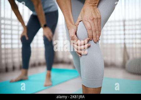 Aspetta solo che smetta di ferire. Primo piano corto di una donna irriconoscibile che sperimenta dolore al ginocchio mentre si esercita a casa. Foto Stock