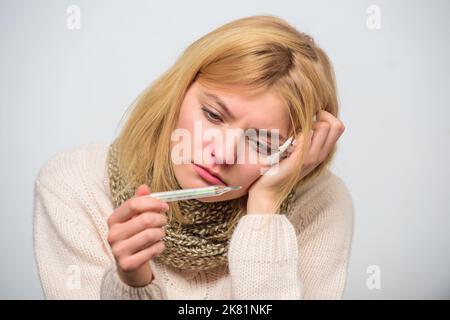 Break febbre rimedi. Prendere la temperatura e valutare i sintomi. Concetto di alta temperatura. La donna si sente male starnutire. Ragazza in sciarpa tenere termometro Foto Stock