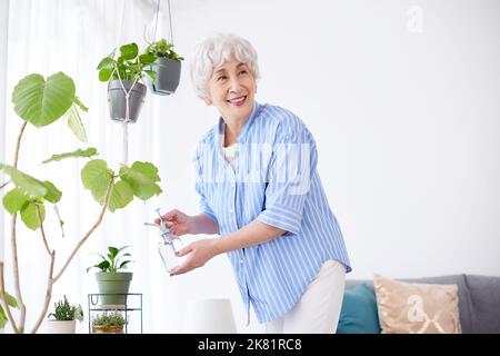 Donna anziana giapponese che innaffia le piante Foto Stock