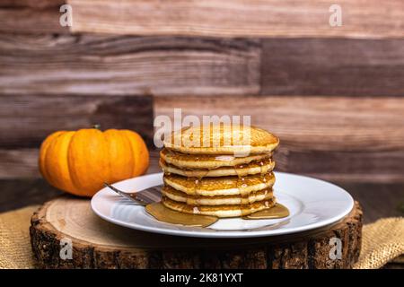 Una pila di frittelle di zucca con sciroppo d'acero su una fetta rustica di legno con spazio copia Foto Stock