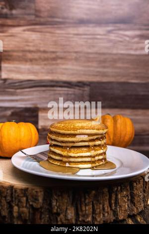 Una pila di frittelle di zucca con sciroppo d'acero su una fetta rustica di legno con spazio copia Foto Stock