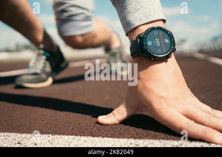 un uomo si sta preparando a iniziare con un tapis roulant. orologio intelligente in mano all'atleta. Applicazioni per smartwatch per l'allenamento all'aperto. Foto Stock