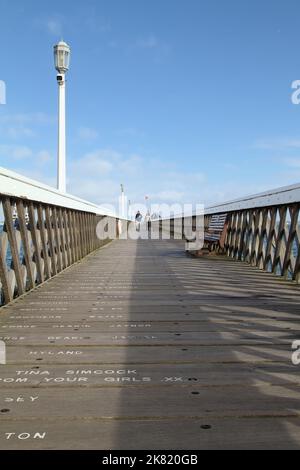 Due persone camminano sul Molo di legno di Yarmouth, Yarmouth, Isola di Wight uk Foto Stock