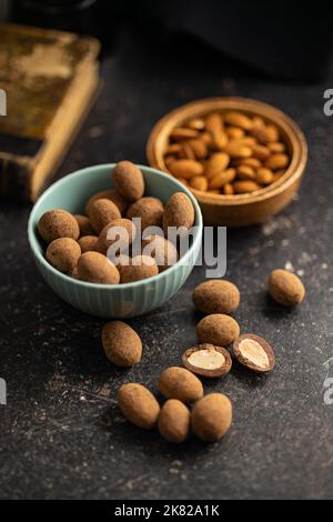 Mandorle in cioccolato ricoperte di cacao in ciotola su un tavolo scuro. Foto Stock
