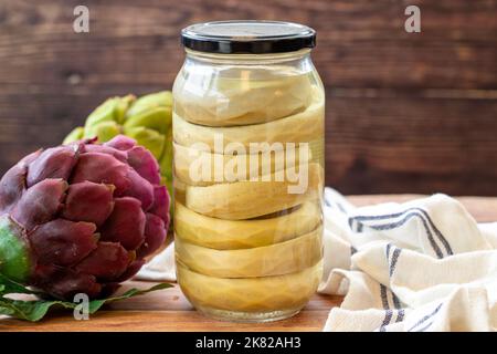 Carciofi in scatola in vaso di vetro su sfondo di legno Foto Stock