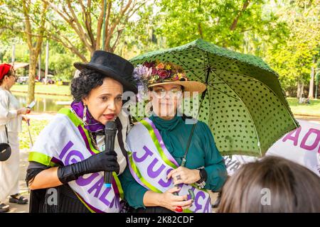 Goiânia, Goias, Brasile – 12 ottobre 2022: Una donna, vestita a suffragetta, che parla nel microfono e un'altra donna che tiene un ombrello. Foto Stock