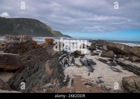 Onde che si infrangono contro rocce che si infrangono sulla costa Foto Stock