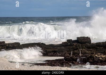 Onde che si infrangono contro rocce che si infrangono sulla costa Foto Stock