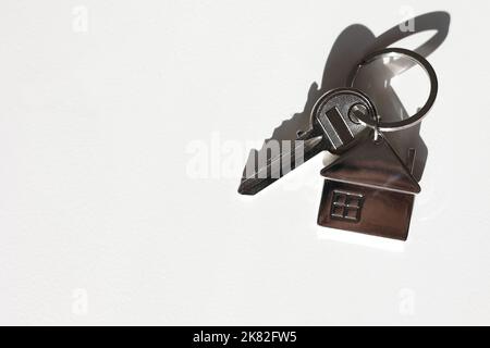 Portachiavi e portachiavi a forma di casa in metallo disposti su sfondo bianco con ombra. Commercio e assicurazione. Concetto di acquisto, vendita, locazione di vera esta Foto Stock
