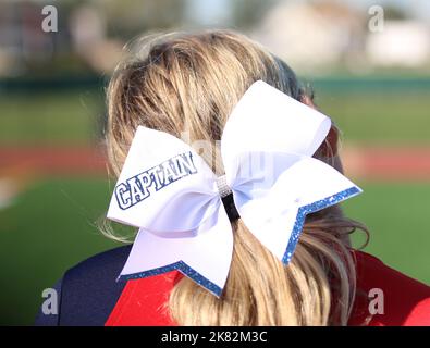 Vista posteriore di un cheerleaders della scuola superiore inchino sulla sua testa bionda che ha capitano scritto su di esso da vicino. Foto Stock