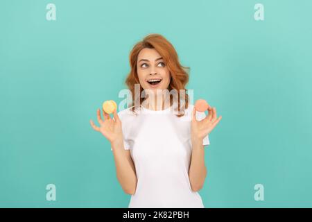 felice donna scioccata tenere dolce biscotto francese macaron su sfondo blu Foto Stock