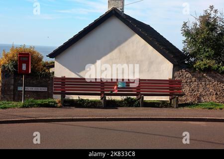 Una lunga panchina sulla strada in cima ad una collina adiacente alla strada principale attraverso il villaggio di Ogmore via mare, un bel posto per sedersi e guardare il mondo andare vicino. Foto Stock