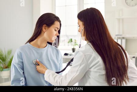Giovane donna caucasica afflitta in esame in clinica privata siede medico di fronte con stetoscopio Foto Stock