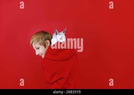 ragazzo vestito con una tuta rossa con un gatto sulle spalle su sfondo rosso Foto Stock