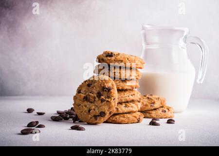 Gustosi biscotti fatti in casa con scaglie di cioccolato e caraffa di latte in vetro su fondo grigio in cemento Foto Stock