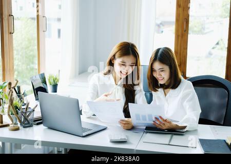 Consulenza, apprendimento, marketing, investimento, finanza, Analisi dei dati, ricerca, due donne asiatiche sorridenti e tenendo documenti, seduti e analizzando Foto Stock