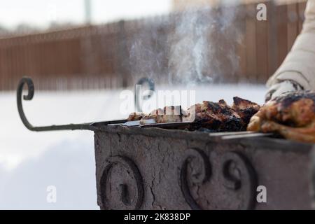 La mano di una donna in un culo fritta un barbecue sulla griglia in natura in una giornata d'inverno soleggiata. Messa a fuoco selettiva. Primo piano Foto Stock