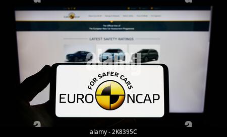Persona che tiene uno smartphone con il logo del programma di sicurezza dell'auto Euro NCAP sullo schermo di fronte al sito Web. Messa a fuoco sul display del telefono.